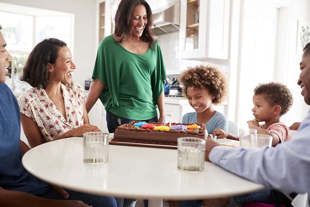 Three generation family mixed race family gathered around the kitchen table celebrating the pre-teen daughterâ€™s birthday with a birthday cake