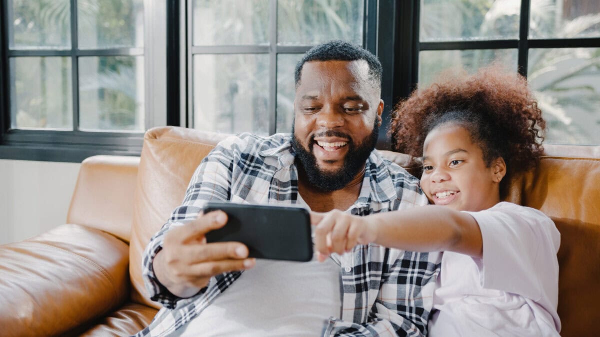 Happy African American family dad and daughter having fun and using mobile phone video call