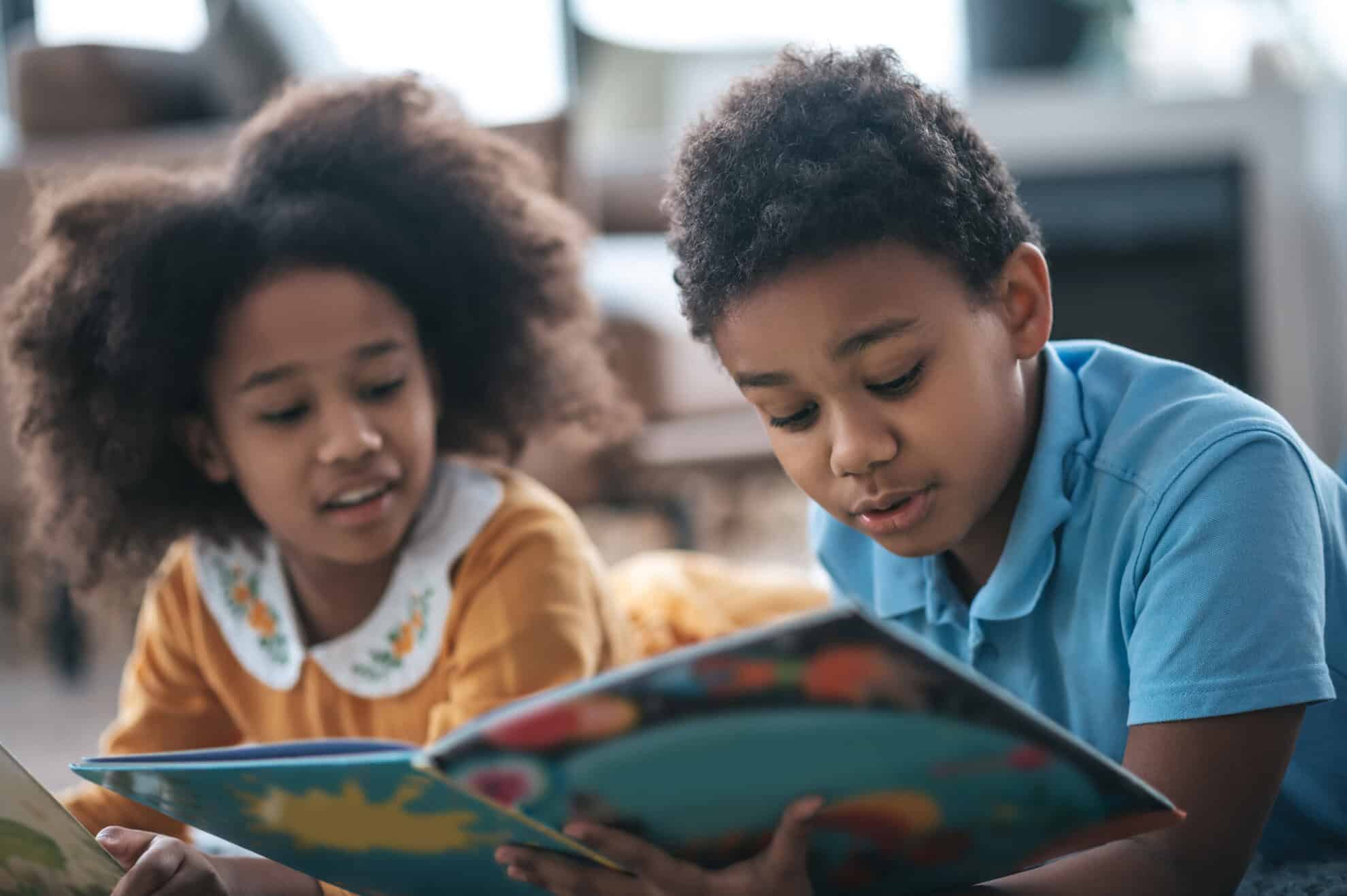 Two kids lying on the floor and reading a book