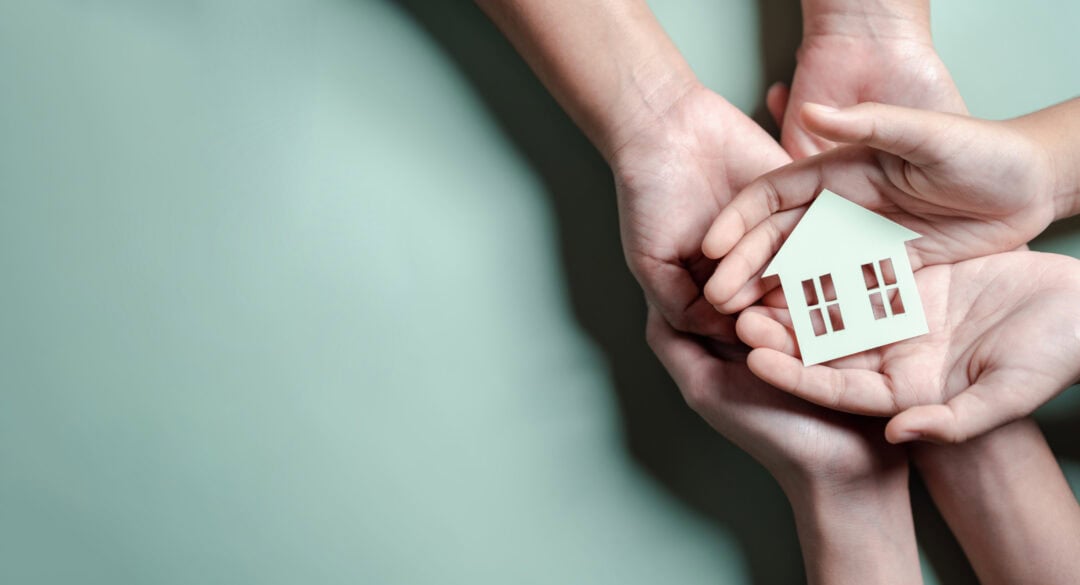 Hands holding a small house model symbolizing child welfare and community support.