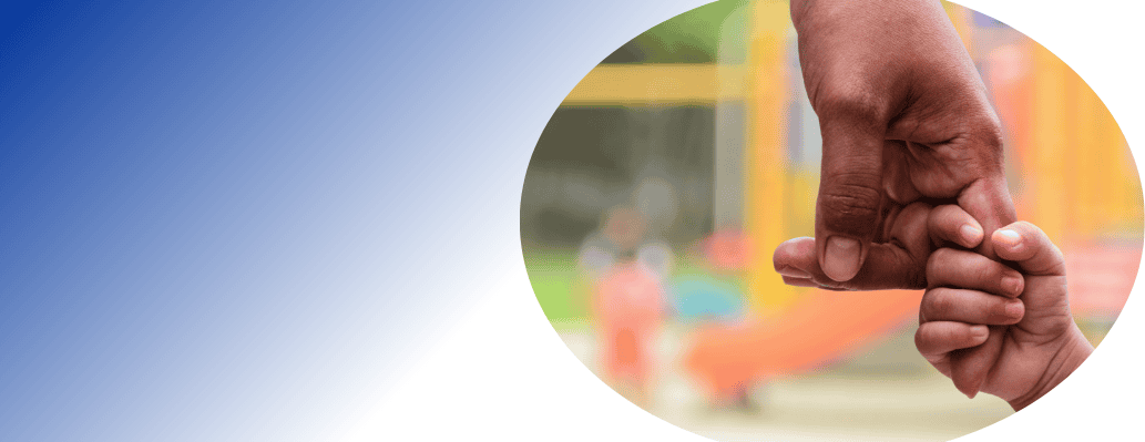 Child's hand holding an adult's finger at a playground.